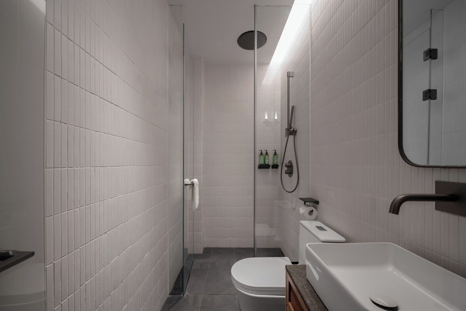 A modern bathroom with white tiles, a glass shower enclosure, a toilet, a sink, and a mirror.
