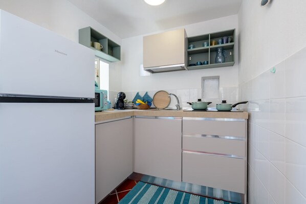 A compact kitchen with white cabinets, a built-in stove, and a microwave. There are shelves above the counter holding various kitchen items.