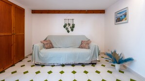Une pièce avec une armoire en bois, un canapé bleu clair agrémenté de deux coussins, une plante suspendue et un tableau encadré au mur.