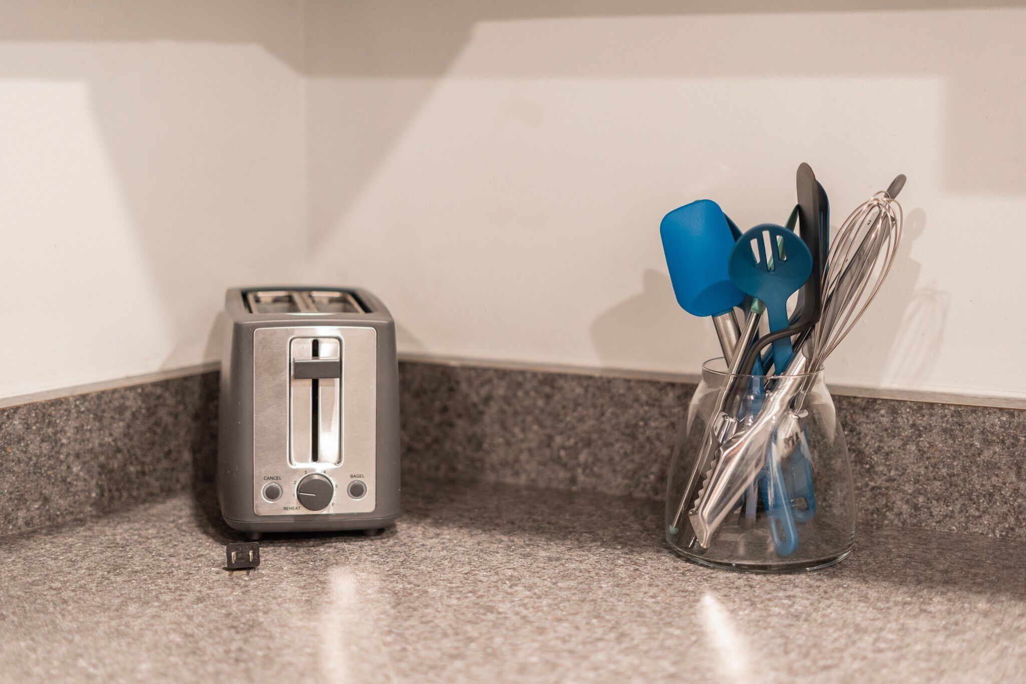 Una encimera de cocina con un tostador y un recipiente de vidrio con utensilios de cocina.