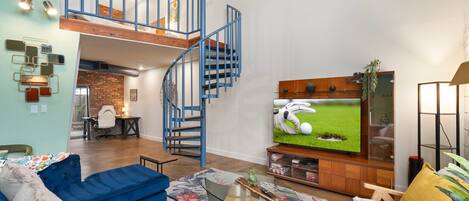 Ein geräumiges Wohnzimmer mit einer blauen Wendeltreppe, einem großen Flachbildfernseher und einer gemütlichen Sitzecke mit blauen Sofas und einem Couchtisch.