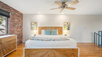 A modern bedroom with a wooden headboard, a bed with a white comforter, two bedside lamps, and a ceiling fan.