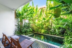 Ein Poolbereich mit Holzstühlen und einem kleinen Tisch, umgeben von üppiger tropischer Vegetation.