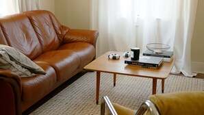 A living room with a brown leather sofa, a wooden coffee table with books and a candle, and a patterned floor.