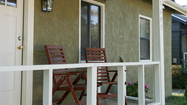 A porch with two wooden chairs and a table, a door, and a window.