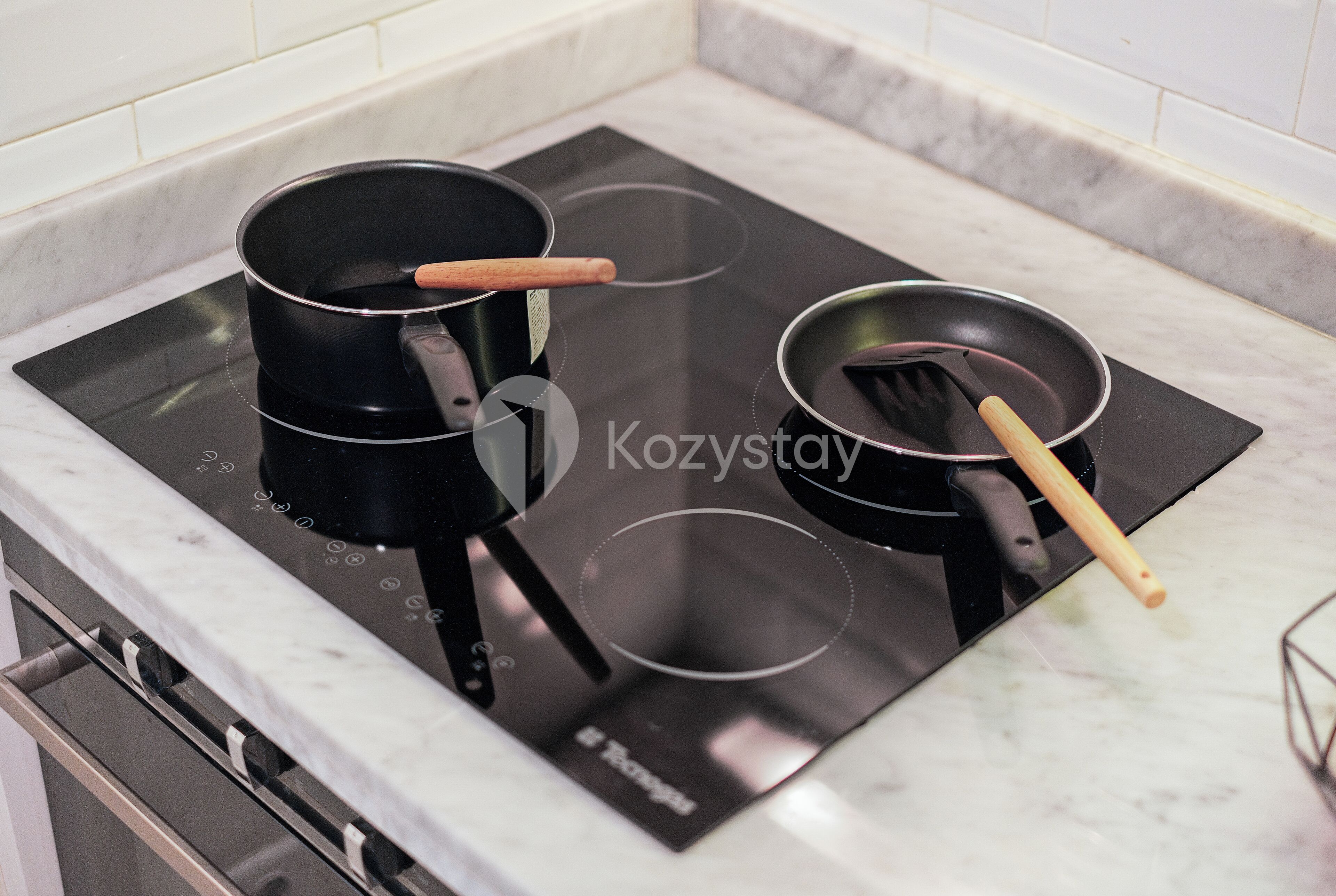 Una cocina con una placa de inducción negra, dos ollas y una sartén con mango de madera.