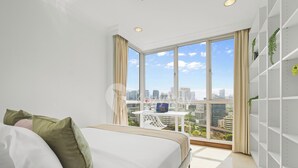 Ein modernes Hotelzimmer mit großem Fenster, einem Bett, einem kleinen Tisch und einer weißen Regaleinheit.