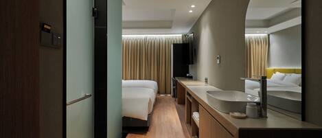 A hotel room with a wooden floor, a large mirror, a sink, a bed, and a window with curtains.