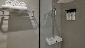 A modern shower area with a glass partition, a towel rack with rolled towels, and a shelf with toiletries. - 88Hotel (Seoul)