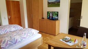 A bedroom with a bed, wooden wardrobe, a television on a table, and a dining area with a table and chairs. - 2 Cozy vacation apartment for 2 persons, 20sqm, balcony or terrace (Bad Reichenhall)