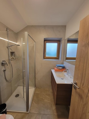 A modern bathroom with a glass-enclosed shower, a vanity with a mirror, and a small window.