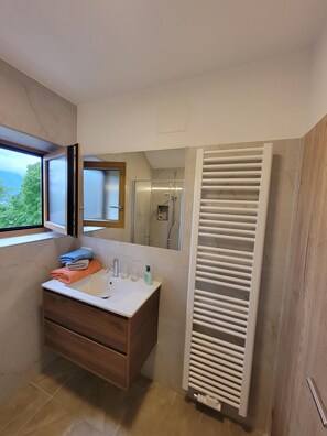 Une salle de bain moderne avec un meuble-lavabo, une douche et une vue sur l’extérieur.