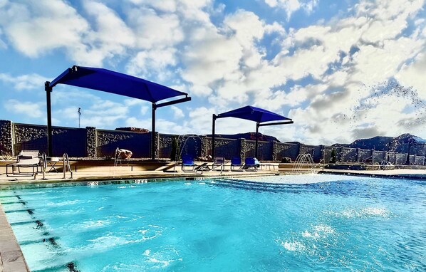 A swimming pool with blue umbrellas, lounge chairs, and a stone wall.