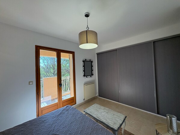 A bedroom with a bed, a bench, a wardrobe, a radiator, and a window with a view of trees.