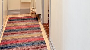 En hall med en färgglad, randig matta, en vit dörr längst ner och två inramade konstverk på väggen.