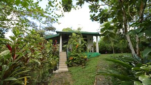 A covered outdoor area with a staircase leading to a covered seating area surrounded by lush greenery and plants. - Sinharaja River Lodge (Kalawana)