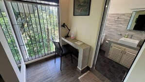 A room with a desk, chair, and a large window with a view of greenery. - Sinharaja River Lodge (Kalawana)