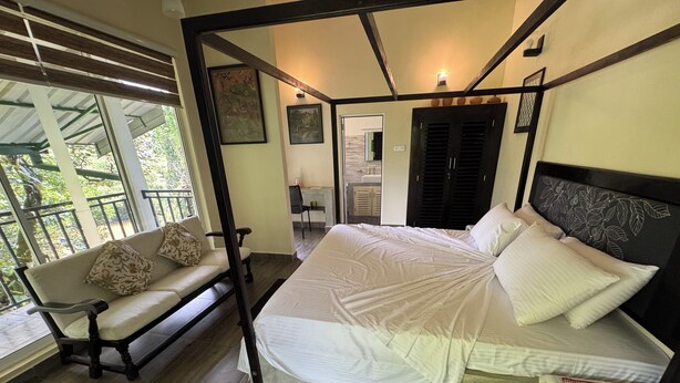 A bedroom with a large bed, a bench with cushions, and a view of the outdoors. - Sinharaja River Lodge (Kalawana)