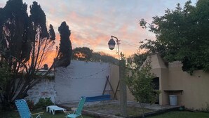 Ein Garten mit zwei Stühlen, einem Tisch, einer hängenden Laterne und einem kleinen Gartenbereich.