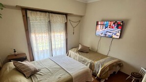 Ein Schlafzimmer mit zwei Betten, einem Fernseher, einem Fenster mit Vorhängen und einer Deckenleuchte.