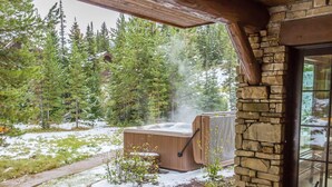 A covered patio with Adirondack chairs, a stone wall, and a hot tub. - Vast Ski In/Ski Out Big Sky Chalet (Big Sky)