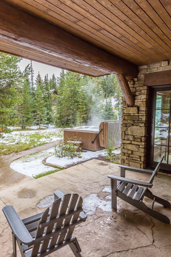 Een overdekt terras met Adirondack-stoelen, een stenen muur en een jacuzzi.