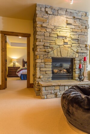 A stone fireplace with a mantel, a wooden bench, and a doorway leading to a bedroom.