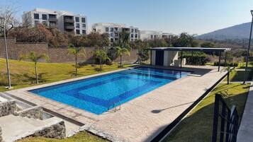 Una piscina rectangular con agua azul cristalina, rodeada por una terraza de piedra y un área con césped.