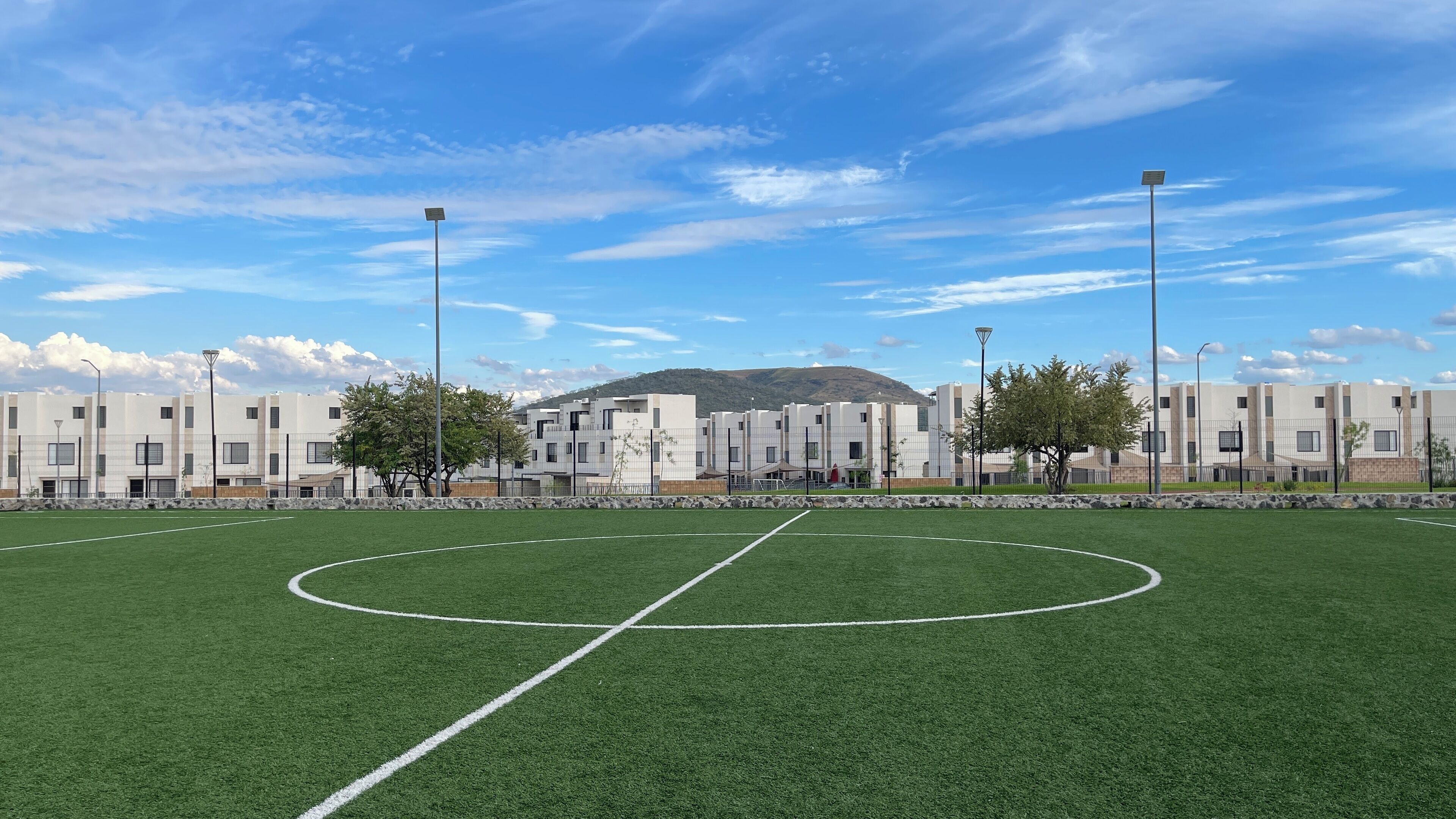 Un campo de fútbol con porterías, rodeado por una cerca y edificios al fondo.