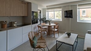 A modern kitchen with white cabinets, a dining area with a round table and chairs, and a TV mounted on the wall.