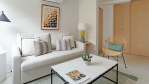 A modern living room with a sofa, a coffee table with a magazine, a lamp, a wicker chair, and a wardrobe.