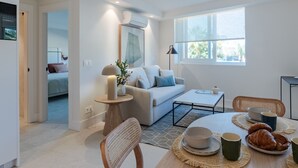 Una sala de estar moderna con sofá, mesa de centro y comedor con individuales y un plato de croissants.