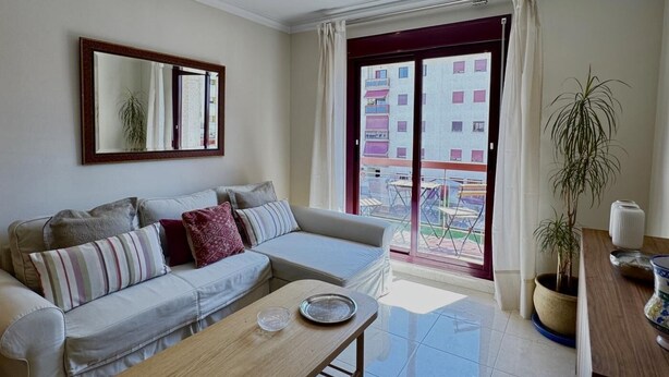 Una sala de estar moderna con un sofá, una mesa de centro, un ventanal con vistas a edificios y una planta en maceta.