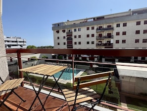 Ein Balkon mit Holztisch und -stühlen, mit Blick auf ein Schwimmbad und ein Wohngebäude.