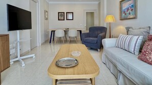 Una sala moderna con televisor, una mesa de centro de madera, un sofá, una silla y una mesa de comedor con sillas.