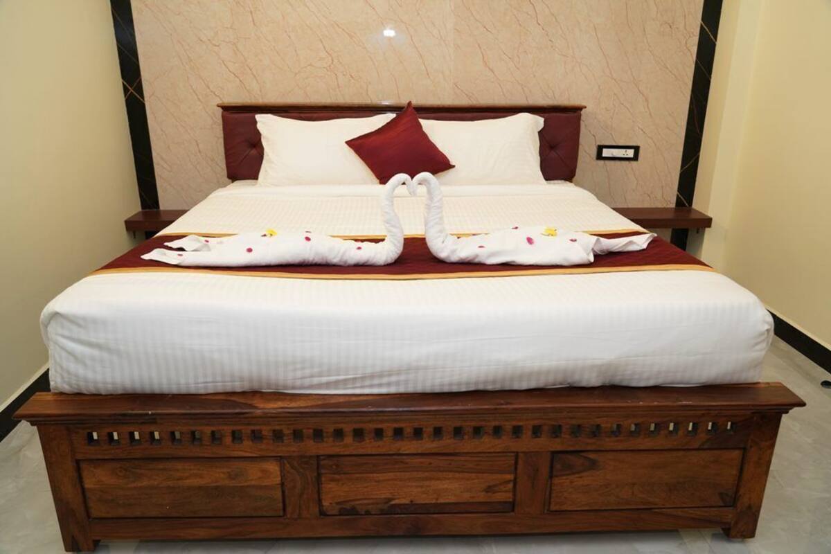 Una cama bien hecha con un almohadón rojo, uno blanco y una decoración de toallas con forma de cisne.