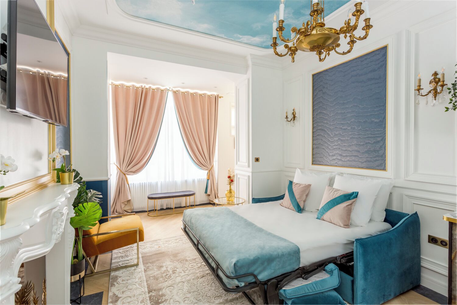 Habitación de hotel con cama, banca, televisor, planta y un cuadro grande en la pared.