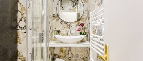 A bathroom with a glass-enclosed shower, a white sink with a marble backsplash, and a gold door handle.