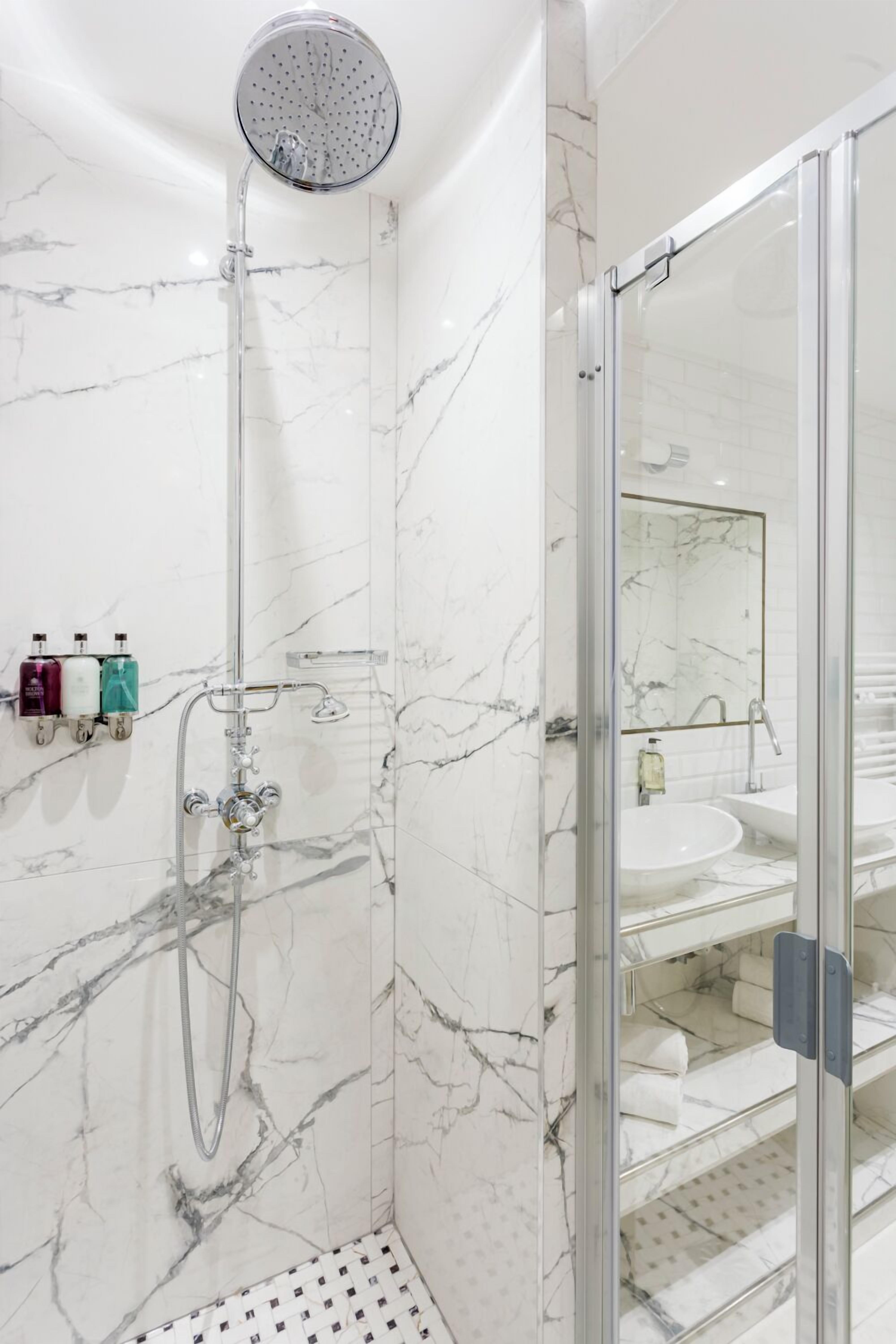 Un baño moderno con ducha de vidrio, paredes de mármol y un espacio visible para el lavamanos.
