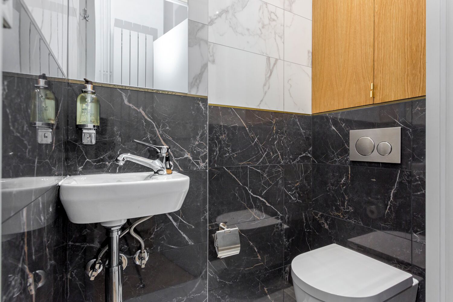 Un baño moderno con lavamanos blanco, paredes cubiertas de mármol y un mueble de madera.