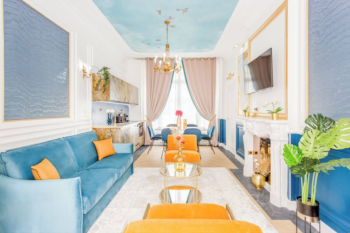 A spacious living room with a blue sofa, orange armchairs, a glass coffee table, and a fireplace.