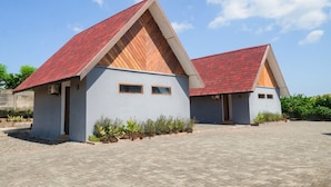 A modern building with a red-tiled roof and a grey facade, featuring two small windows and a paved entrance area. - Seaside Sayang Heulang by Sinergi (Pameungpeuk)