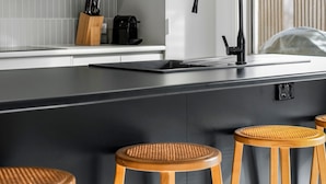 Een moderne keuken met grijze kastjes, een zwart aanrecht en houten krukken.