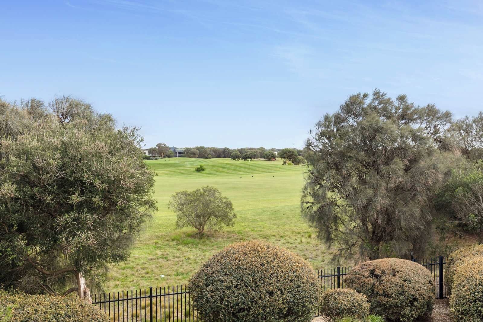 Ein Golfplatz mit Zaun, Bäumen und einem Gebäude im Hintergrund.