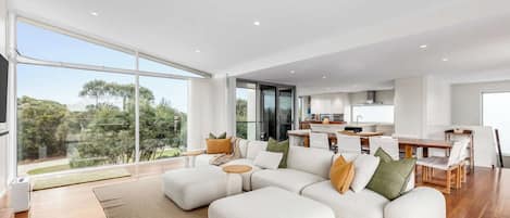 A modern living room with a sectional sofa, a dining area, and a kitchen.