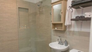 Ett badrum med en dusch som är avskärmad med glasväggar, ett handfat på en piedestal, en toalett och en handdukshängare med hopvikta handdukar.