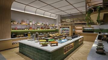 A modern buffet setup with various food items and drinks, a green-tiled backsplash, and a wooden floor.
