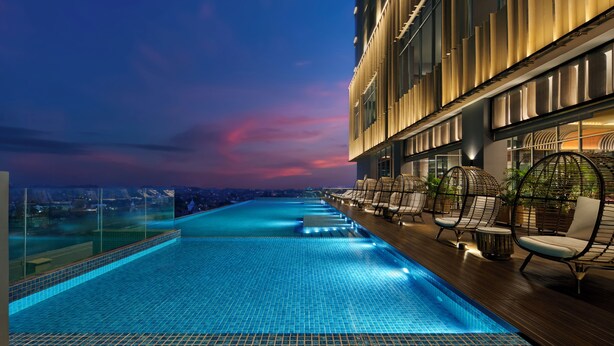 A rooftop infinity pool with a city view, lounge chairs, and a modern building facade.