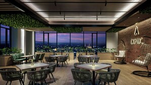 A modern dining area with tables and chairs, large windows with a city view, and a brick wall with a sign.
