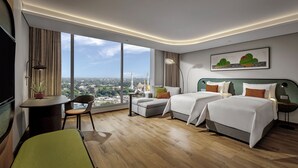 A hotel room with two beds, a desk, a chair, and a large window offering a city view.